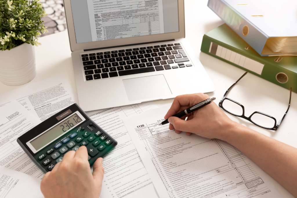 Person filling out tax forms with a laptop and calculator on the table