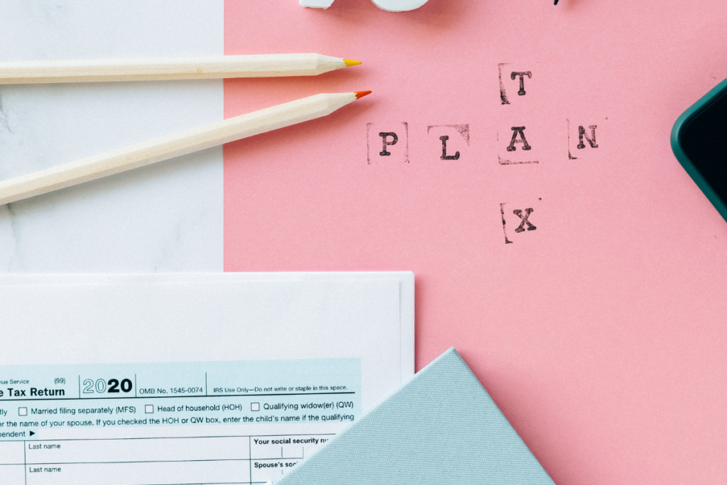 "Plan Tax" written on a pink paper surrounded by tax forms and pencils
