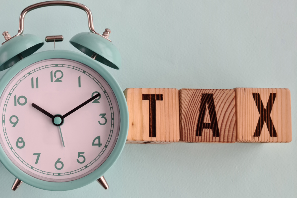 Wooden cube with "Tax" written on it next to an alarm clock