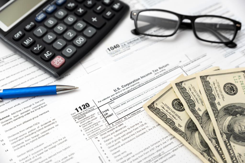 Tax forms with a money calculator and eyeglasses on the table
