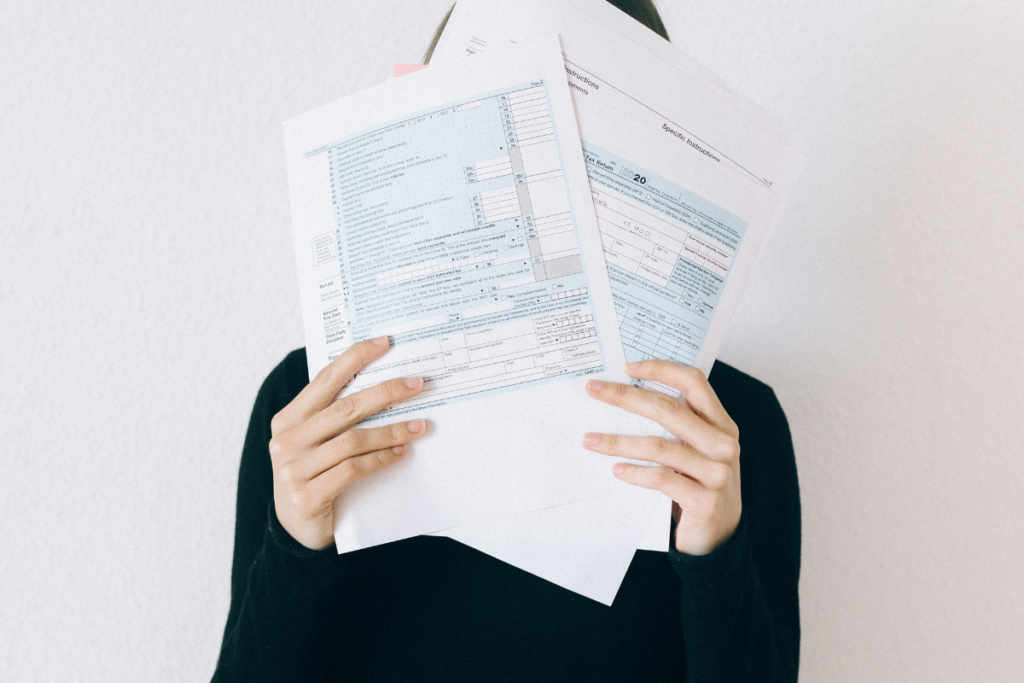 A woman covering her face with tax forms, appearing distressed
