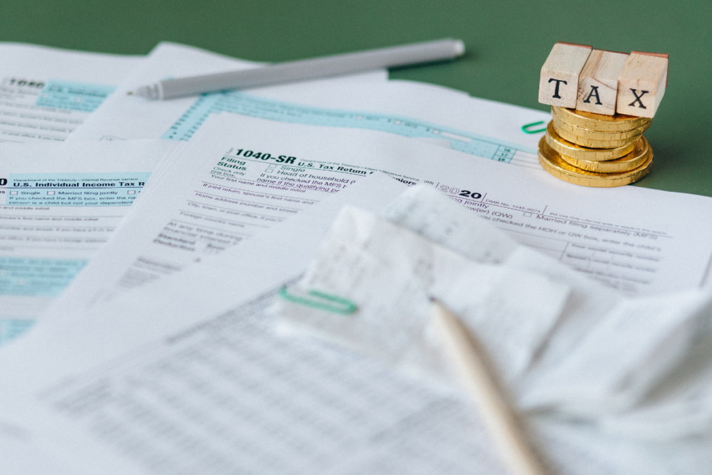 Tax forms on a table with a wooden cube labeled "Tax" and gold coins
